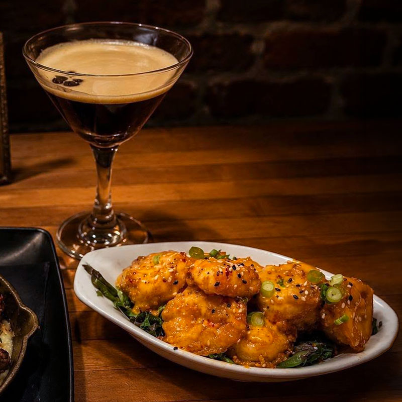 Golden-Hemline-Cocktail A plate of buffalo chicken wings with a Midnight Stitch cocktail